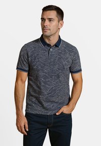 Marineblauwe polo met een wit bladdessine, korte mouwen en een contrasterende kraag. Gladde textuur en slim fit. Minimaal accent.