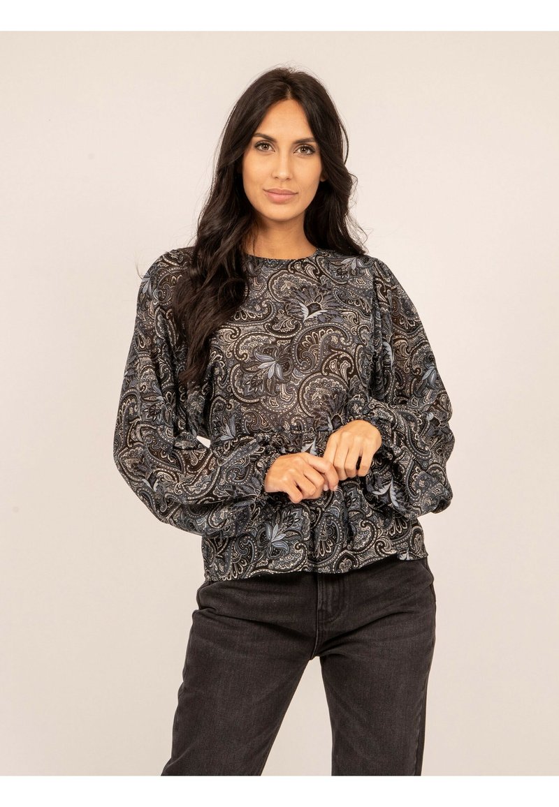 Blouse noire à motif paisley avec des manches bouffantes et un ourlet froncé. Tissu doux avec des détails floraux complexes en bleu et gris. Portée avec un jean foncé.