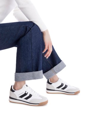 Zapatillas blancas y grises con rayas negras, con cordones, que presentan un acabado de ante texturizado y suelas de goma. Los recortes en los laterales mejoran el diseño.