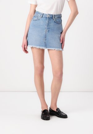Lyseblå denim miniskjørt med nedre søm som er slitt, fem lommer og knappestenging; brukt sammen med en enkel hvit skjorte og svarte loafers.