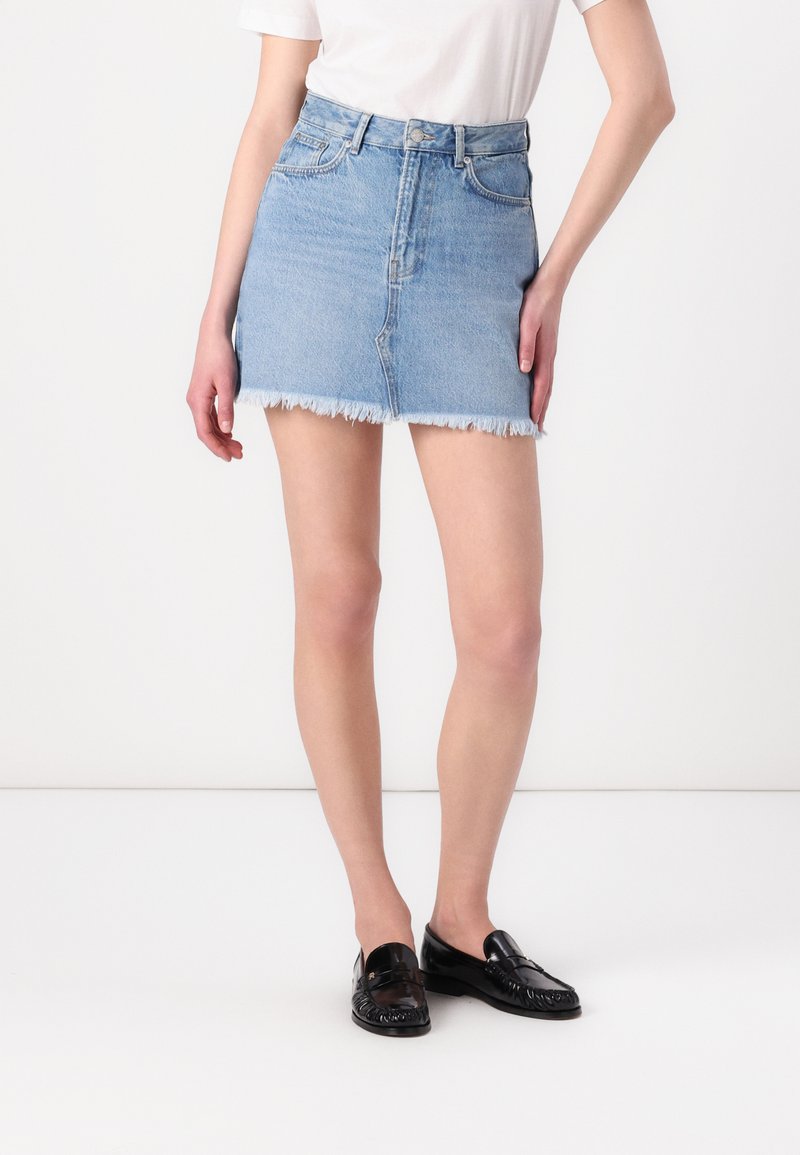Ljust blå denim mini kjol med fransade kanter, femficksdesign och knäppning; bärs med en enkel vit skjorta och svarta loafers.