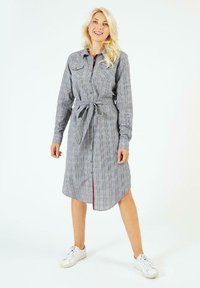Robe à carreaux gris avec des manches longues, un boutonnage à l'avant, des poches poitrine et une taille cintrée ; présente un ourlet incurvé et des détails en accent rouge.