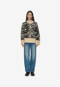 Sort og beige fuzzy sweater med tigerstriber, rund hals og brede manchetter, parret med blå løstsiddende jeans og sort fodtøj.