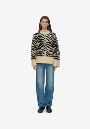 Juodas ir smėlio spalvos pūkuotas megztinis su tigro raštais, apvalia iškirpte ir plačiomis rankovėmis, derinamas su mėlynomis laisvomis džinsomis ir juodais batais.