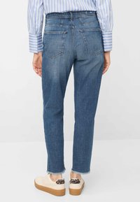 Spijkerbroek met taps toelopende pasvorm, mediumblauwe kleur en vijf zakken. Ongezoomde zoomdetail bij de enkel. Gecombineerd met crèmewitte sneakers met een luipaardprintaccent.