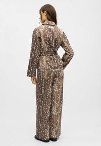 Braun gemustertes Anzugset mit einem Gürtel in der Taille und weit geschnittenen Hosen. Der Stoff weist ein rehähnliches Muster mit crèmefarbenen Akzenten und einer glatten Textur auf.