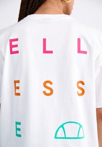 White cotton t-shirt featuring multicolored text: pink "EL," orange "ES," and green graphic accent. Simple design with a relaxed fit.