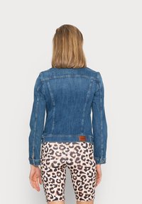 Jeansjacka i medelblått med klassisk snitt, sidofickor och en brun läderlapp på baksidan. Matchad med leopardmönstrade shorts.