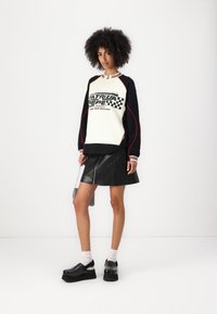 Sweatshirt bianco e nero con testo grafico, abbinato a una gonna in pelle nera con zip frontale. Scarpe con tacco nero e calze bianche.