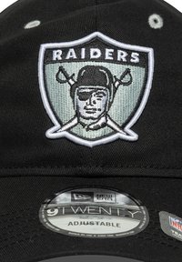 Melnā regulējam�ā cepure ar Raiders logo, kas ietver izšūtu dizainu ar bruņota figūru un šķēpiem, kas krustoti uz gaiša vairoga fona.