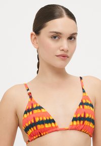 Driehoekige bikini top in een levendig rood, geel en blauw tie-dye patroon. Voorzien van dunne bandjes en decoratieve kralen op de schouderbandjes.