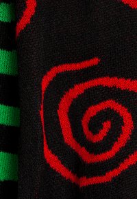 Tessuto in maglia nera con un audace motivo a spirale rosso, completato da accenti strizzati verdi e neri. Texture morbida con un netto contrasto di colori.