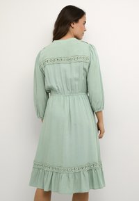 Mint green dress with three-quarter sleeves, a cinched waist, and lace detailing along the back and hem, featuring a flared skirt.