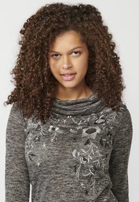 Graues Longsleeve-Oberteil mit Kragen, das auf der Vorderseite mit aufwendiger weißer und schwarzer Blumenstickerei verziert ist. Weicher, strukturierter Strickstoff.