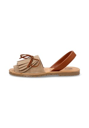 Sandalia deslizante de ante beige con acento de flecos y tira elástica trasera marrón. Suela plana con agarre texturizado y plantilla con marca.