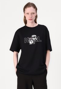 Black cotton t-shirt featuring a graphic print of two cartoon characters. Short sleeves, round neck, casual fit. Suitable for relaxed wear.