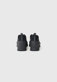Black athletic shoes with a smooth texture, featuring a molded heel with logo and pull tabs for easy wear. Design is streamlined and minimalistic.