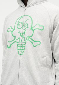 Γκρι φούτερ με φερμουάρ και μεγάλο πράσινο σχέδιο κρανίου παγωτού. Διαθέτει μαλακή υφή, τσέπη καγκουρό και ριμπ μανσέτες.