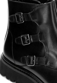 Stivaletto alla caviglia in pelle nera con tre fibbie argentate regolabili e suola spessa e texturizzata.