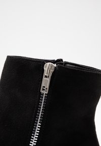 Černé semišové kotníkové boty se stříbrným kovovým zipem na boku a hladkým povrchem, s elegantním minimalistickým designem.