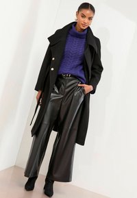 Melns mētelis ar zelta pogām, purpura krāsas adīts džemperis un melnas mākslīgās ādas platjaka bikses. Kopumā veidojas teksturēts slāņots izskats.