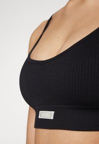 Black ribbed sports bra with narrow straps, a scoop neckline, and a logo tag at the hem. Soft texture and fitted design.