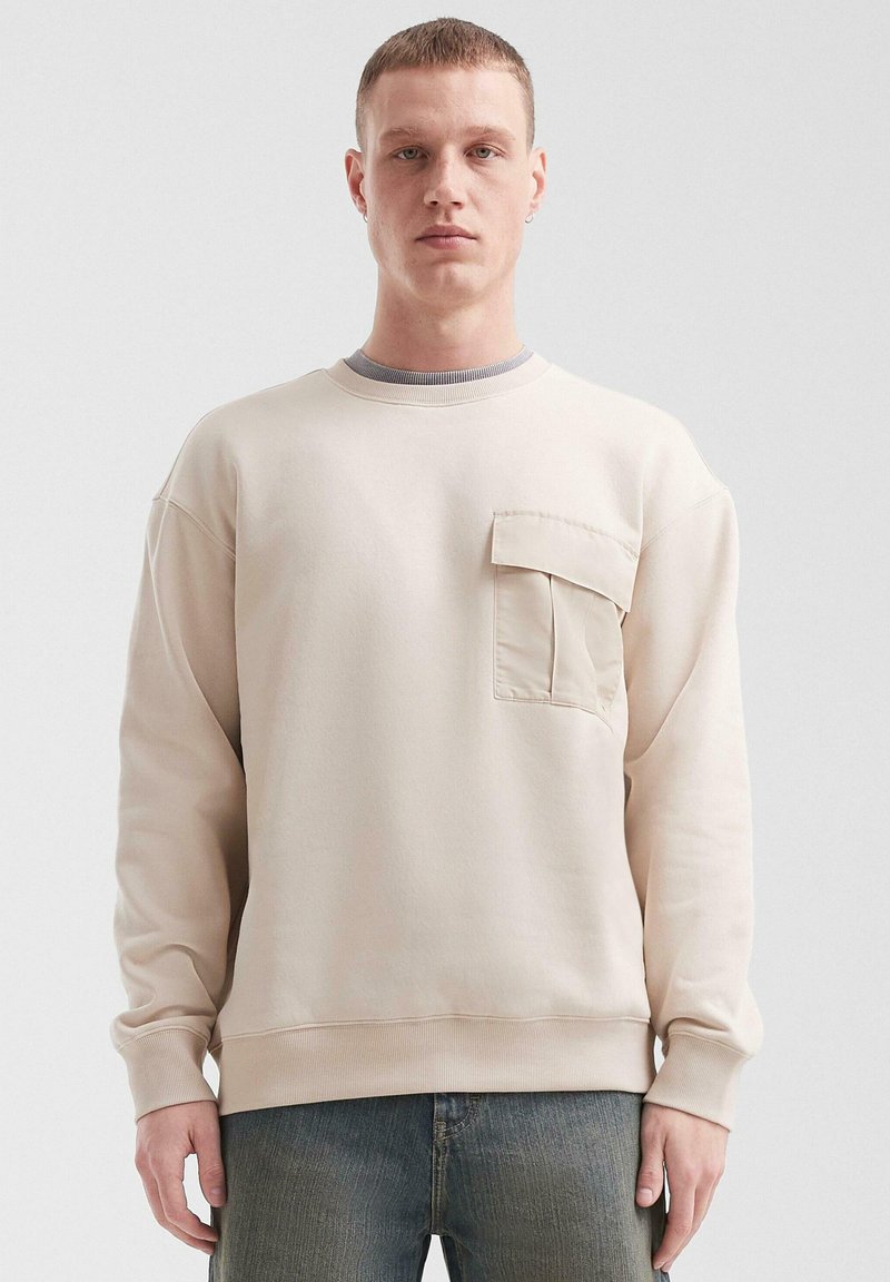 Lichtbeige sweatshirt van zachte stof, met een ronde hals, lange mouwen en een borstzak. Glad textuur en een ontspannen pasvorm.