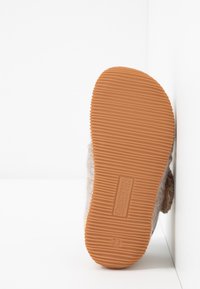 Brązowa gumowa podeszwa z pionowymi rowkami, szara filcowa część górna, zaokrąglony kształt i mała metka z wytłoczonym napisem "Gilles W. Z." na spodzie.