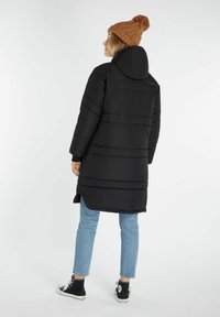 Sort polstret jakke med hætte, med vandret syninger. Parret med lyseblå jeans og sorte sneakers, toppet med en brun strikket beanie.