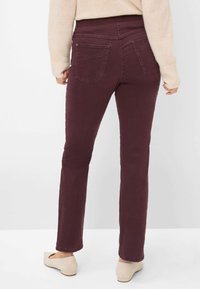Burgundy lige-benet jeans med en mellemhøj talje, fem lommer og lette stikninger. Bæres med en lys beige sweater og flade sko.