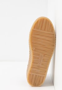 Semelle en caoutchouc brun clair avec motif de texture antidérapante, nom de la marque Gabor et taille 4½ visibles, positionnée à la verticale contre un mur blanc.