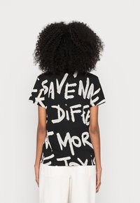 Czarny t-shirt z wyraźnymi białymi napisami, krótkimi rękawami i luźnym krojem. Materiał wydaje się miękki i gładki.