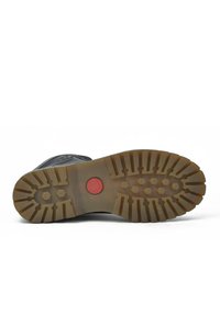 Suela de bota de goma negra con texturas en los tacos y un detalle circular rojo, que presenta patrones hexagonales y lineales para mejorar el agarre.