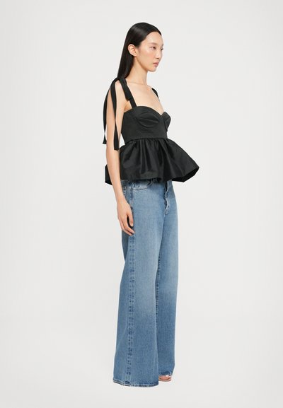 Black peplum top with padded bust and adjustable ribbon straps, paired with wide-leg blue denim jeans. Smooth fabric texture, clean design.