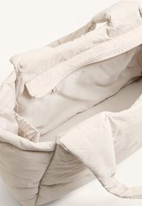 Beige polstret totebag med lynlåsåbning, blød tekstur og stofhåndtag. Indvendigt er den foret med et glat materiale.