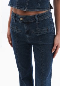 Vaqueros de mezclilla azul oscuro con piernas rectas, una cinturilla ajustada, dos bolsillos delanteros y costuras decorativas a lo largo de las costuras.