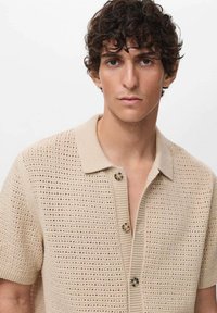 Beige knitted short-sleeve polo shirt with a textured pattern, featuring a collar and three-button closure on a straight cut.