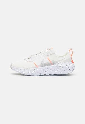 Chaussure de sport blanche avec semelle tachetée, tige en mesh, languette de talon orange et logo swoosh gris, vue de côté sur fond blanc.