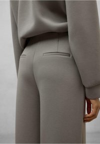 Pantaloni in misto cotone grigi con una texture liscia, dotati di due tasche posteriori su misura e una vestibilità rilassata, abbinati a un top a maniche lunghe coordinato.