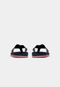 Black flip-flops featuring a textured strap and a multi-layered sole with red and white accents. Open-toe design with no closure.