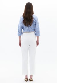 Chemise rayée bleu et blanche aux manches retroussées, assortie à un pantalon taille haute blanc et des sandales à talons dorés, vue de dos.