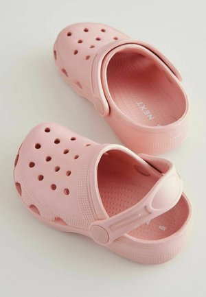 Rozā plastmasas koka kurpes ar ventilācijas caurumiem, aizmugurējo siksniņu un teksturētu zoli. Apaļa purngala forma un gluda apdare.