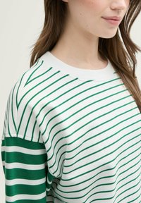 Suéter a rayas verdes y blancas con cuello redondo, fabricado en suave algodón, y detalles en verde que contrastan en las mangas.