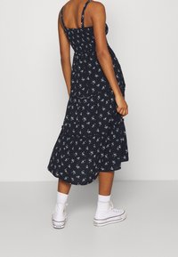 Svart blommig midiklänning med justerbara spaghetti-remmar, lagerdesign, volangkant, ihop med vita sneakers och ankelsockor.