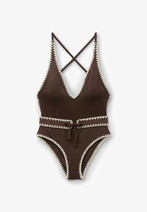 Costume intero marrone testurizzato con bordo bianco smerlato, profonda scollatura a V, spalline incrociate sulla schiena e cintura annodata in vita.