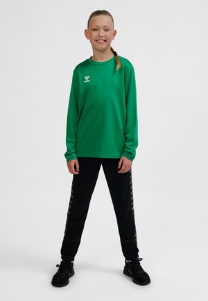 Grøn langærmet sportstop med logo, kombineret med sorte træningsbukser med stribet mønster på siderne. Ensfarvede sorte sportssko.