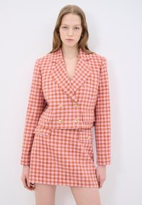 Dwurzędowa marynarka w różowo-pomarańczowy wzór houndstooth z złotymi guzikami, w zestawie z dopasowaną mini spódnicą. Teksturowany materiał, dopasowany krój.