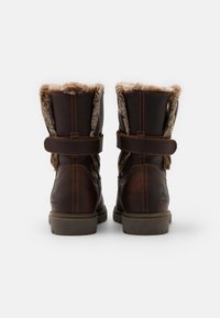Bottes chelsea en cuir marron avec une doublure en fourrure douce, dotées d'une sangle en velcro et d'une semelle en caoutchouc robuste. Le design est pratique et isolé.
