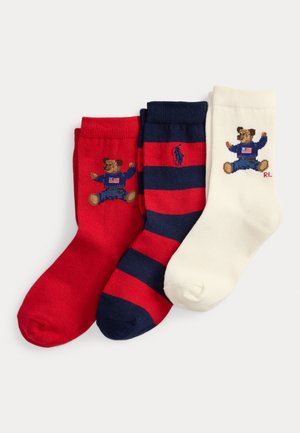 Trois paires de chaussettes : rouges avec un ours brodé, rayées bleu marine et rouges, et crème avec un ours. Fabriquées en tissu doux, avec des bords côtelés.