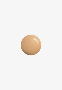 Échantillon de maquillage beige crémeux en forme ronde avec une texture lisse et une légère brillance, sur un fond blanc.